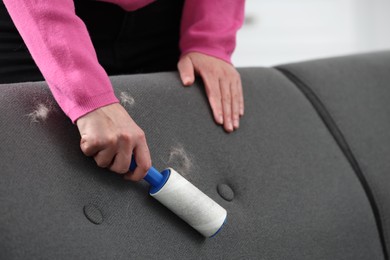 Photo of Woman with lint roller removing pet hair from sofa at home, closeup