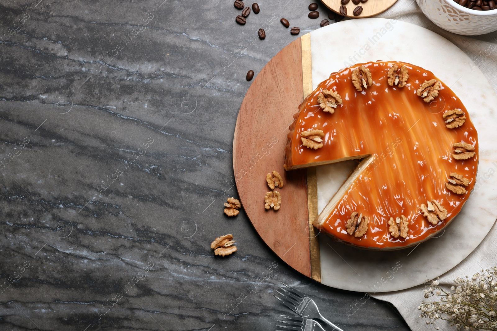 Photo of Delicious cheesecake with caramel and walnuts on black marble table, flat lay. Space for text