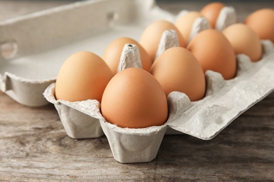 Carton of eggs on wooden table, closeup view