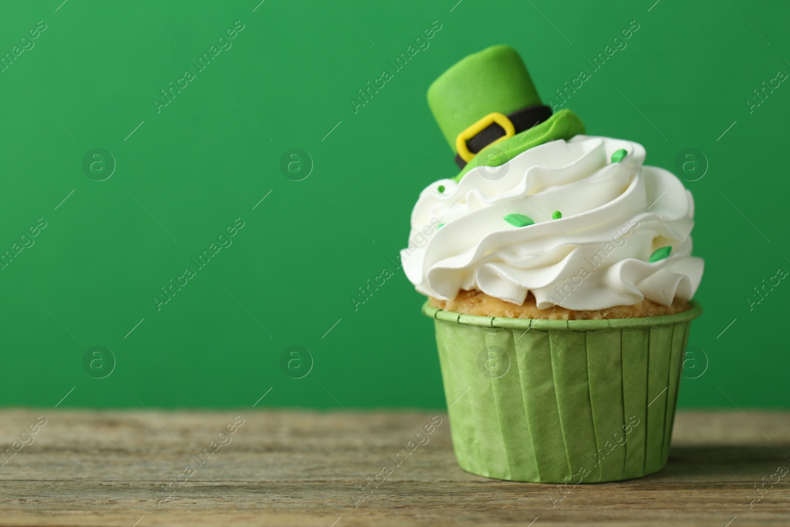 Photo of St. Patrick's day party. Tasty cupcake with leprechaun hat topper on wooden table, closeup. Space for text