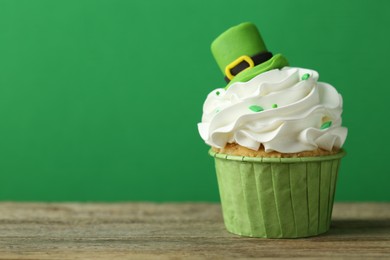 Photo of St. Patrick's day party. Tasty cupcake with leprechaun hat topper on wooden table, closeup. Space for text