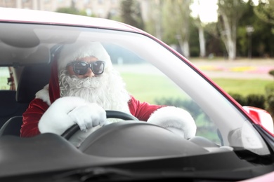 Authentic Santa Claus in sunglasses driving car, view from outside