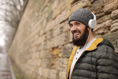 Photo of Mature man with headphones listening to music near stone wall. Space for text