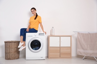 Photo of Young woman sitting on washing machine at home, space for text. Laundry day