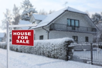 Sale sign near beautiful house outdoors in winter. Red signboard with words