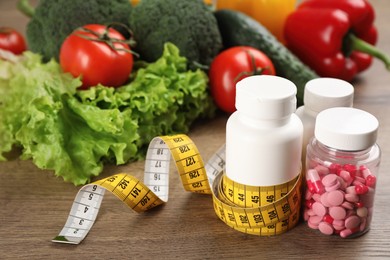 Weight loss pills, different vegetables and measuring tape on wooden table