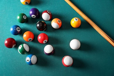 Many colorful billiard balls and cue on green table, above view