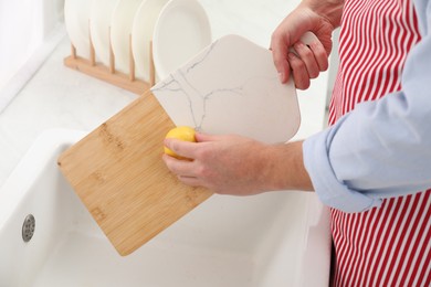 Photo of Man rubbing cutting board with lemon at sink in kitchen, closeup