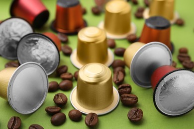 Many coffee capsules and beans on green background, closeup