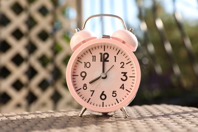 Photo of Pink alarm clock on table outdoors at sunny morning