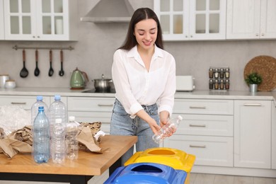 Garbage sorting. Smiling woman throwing plastic bottle into trash bin in kitchen