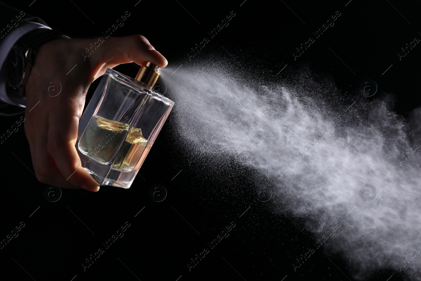 Photo of Man spraying luxury perfume on black background, closeup