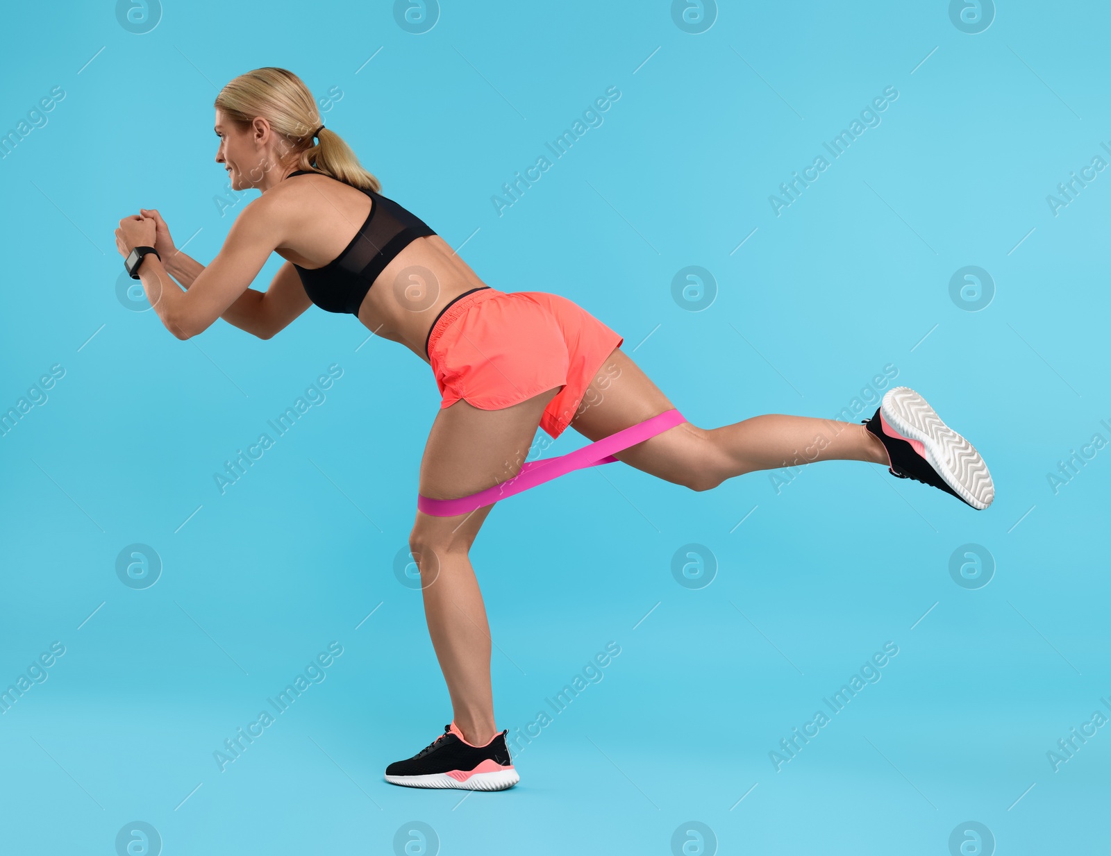 Photo of Woman exercising with elastic resistance band on light blue background