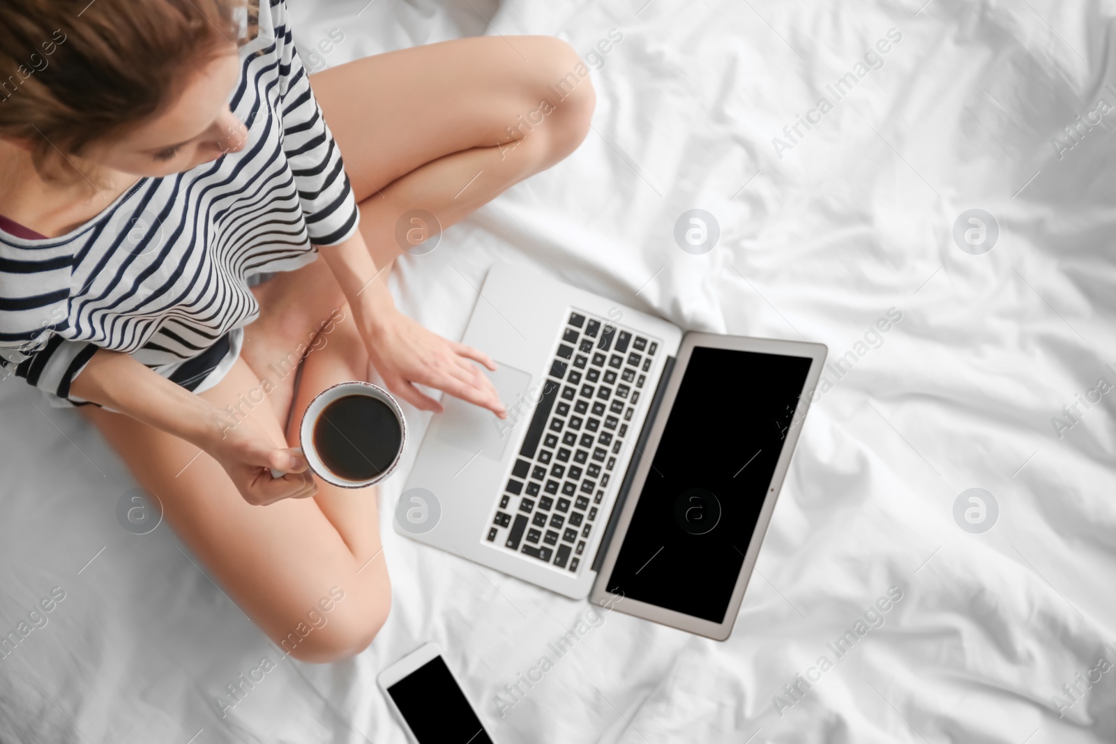 Photo of Female blogger with laptop and cup of coffee on bed, top view