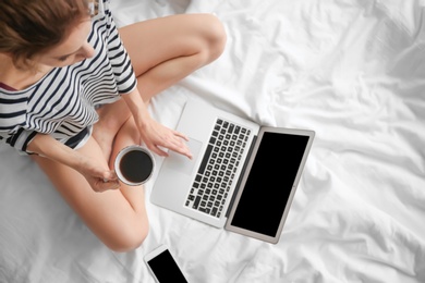 Photo of Female blogger with laptop and cup of coffee on bed, top view