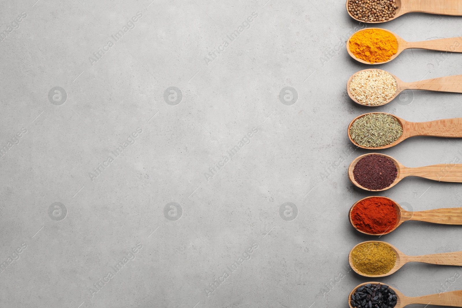 Photo of Flat lay composition with different aromatic spices in wooden spoons on gray background