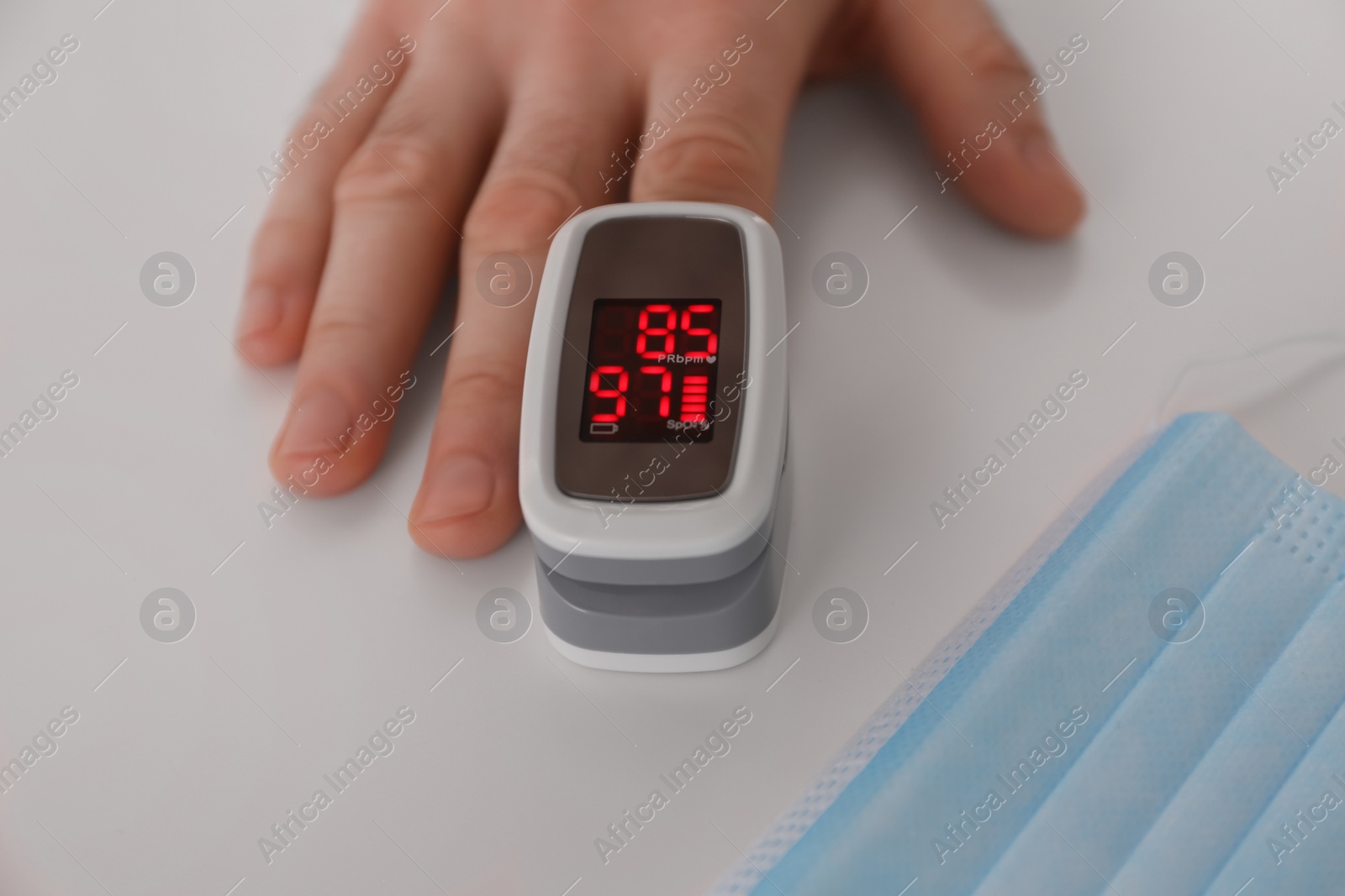 Photo of Man measuring oxygen level with modern fingertip pulse oximeter at white table, closeup