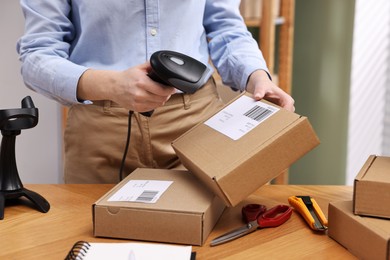 Photo of Parcel packing. Post office worker with scanner reading barcode at wooden table indoors, closeup