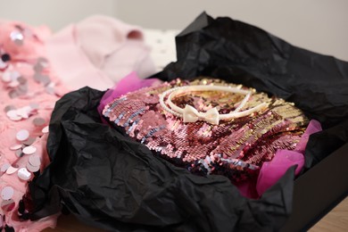 Photo of Headbands and stylish pink carnival costume with sequins in black box on table, closeup