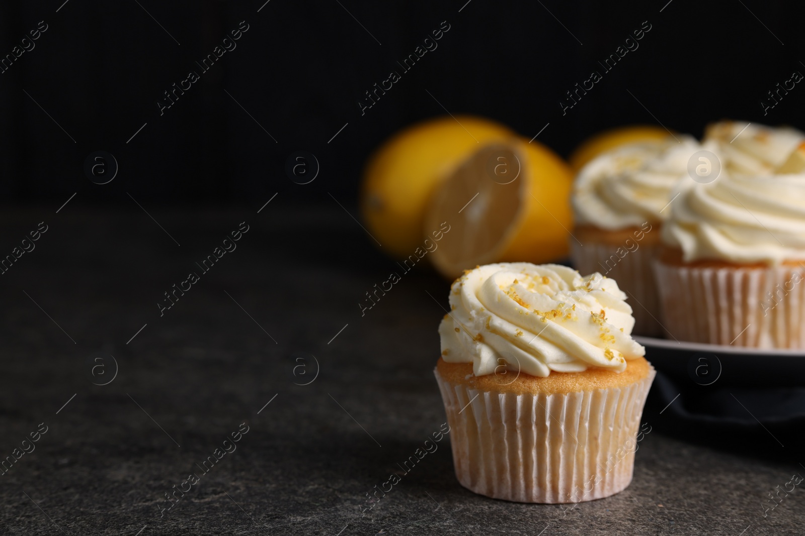 Photo of Delicious cupcake with white cream and lemon zest on gray table, closeup. Space for text