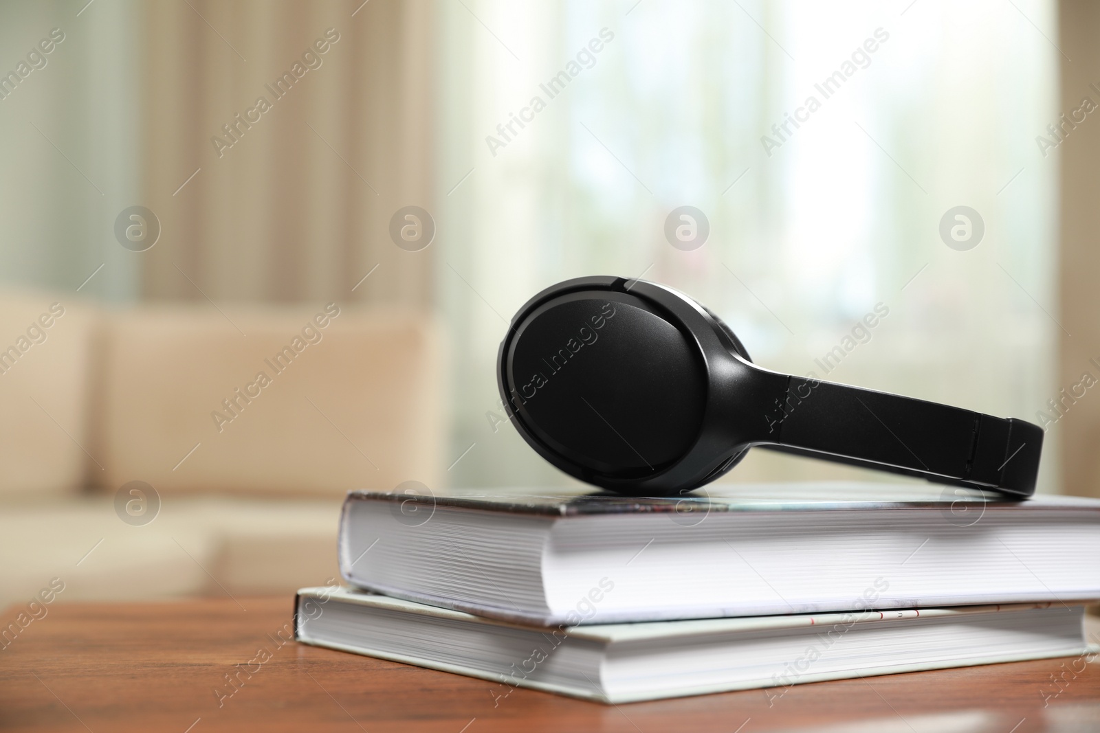 Photo of Modern wireless headphones and books on wooden table indoors