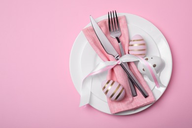 Photo of Festive table setting with painted eggs and cutlery on pink background, top view. Easter celebration