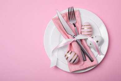 Festive table setting with painted eggs and cutlery on pink background, top view. Easter celebration