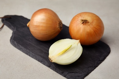 Photo of Slate board with ripe onions on grey table