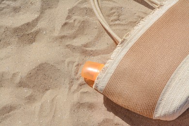 Photo of Closeup view of straw bag with sun protection product on sand, space for text. Beach accessories