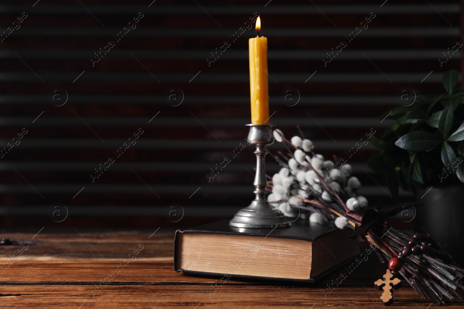 Photo of Rosary beads, Bible, burning candle and willow branches on wooden table. Space for text