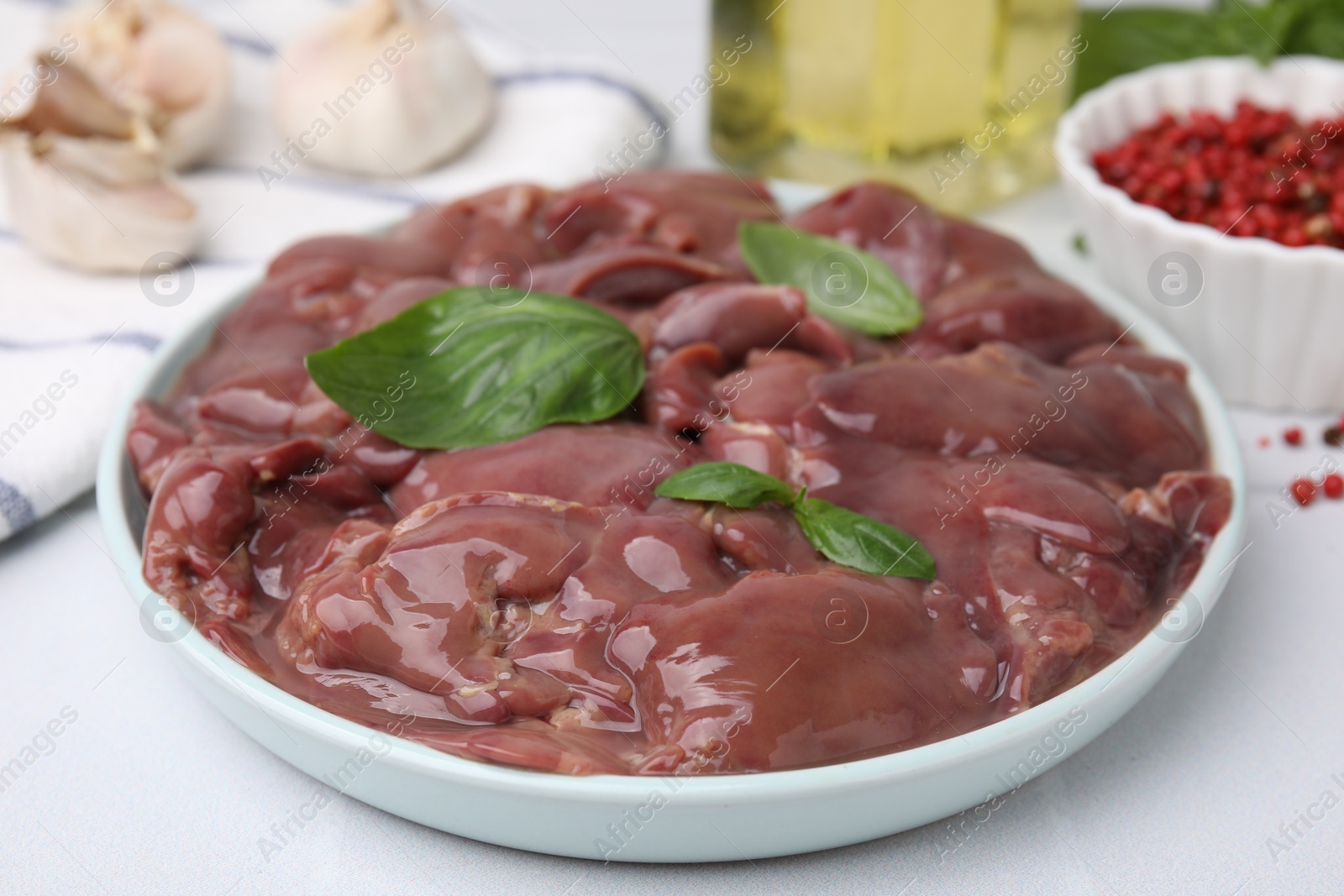 Photo of Plate of raw chicken liver with basil on white table, closeup