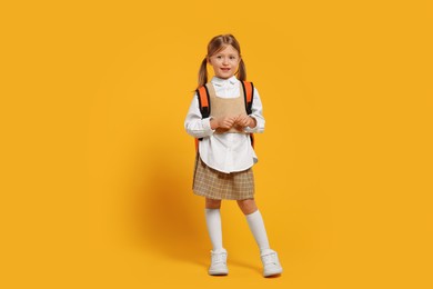 Photo of Happy schoolgirl with backpack on orange background