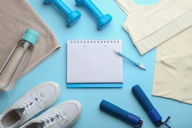 Photo of Flat lay composition with sportswear, notebook and dumbbells on light blue background, space for text. Gym workout plan