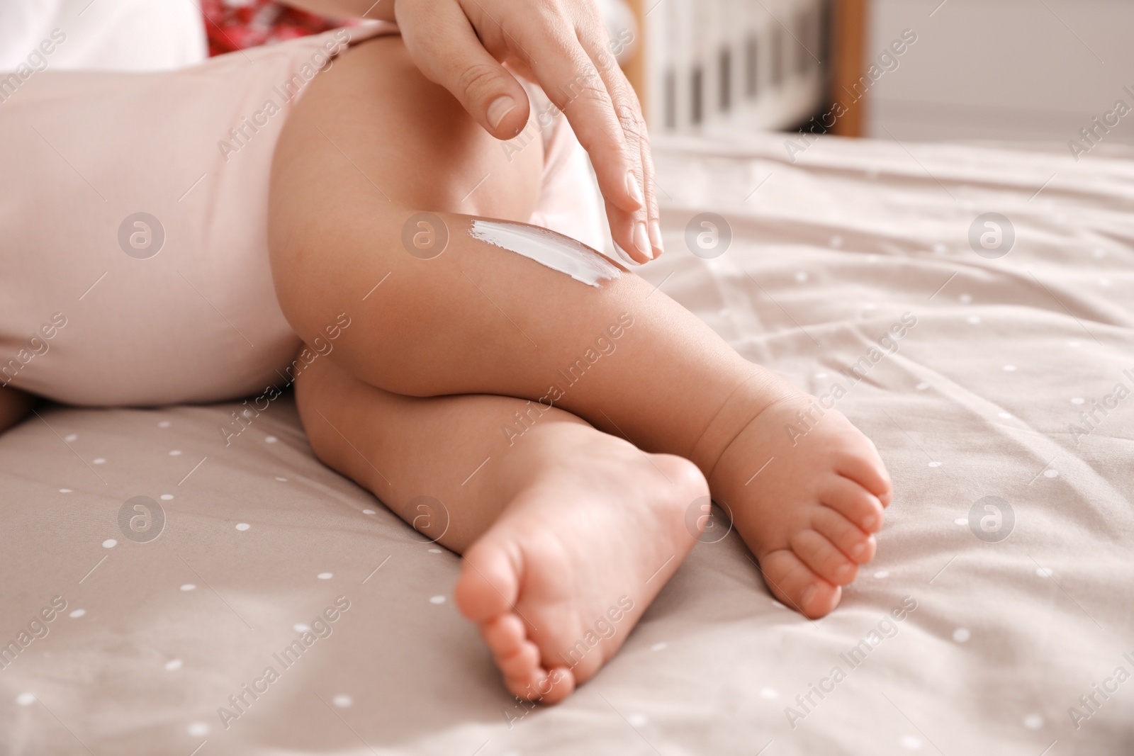 Photo of Mother applying moisturizing cream on her little baby at home, closeup