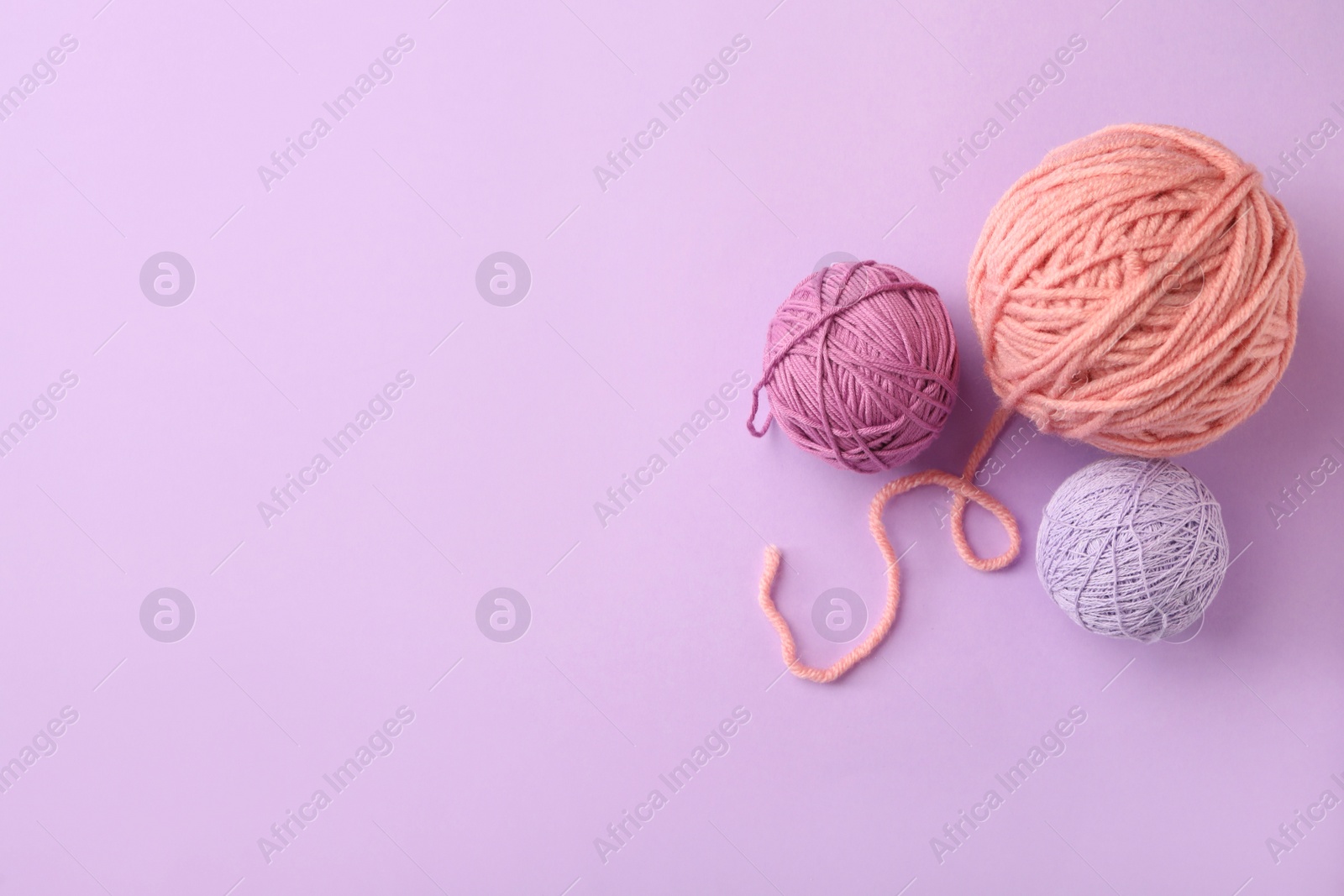 Photo of Soft colorful woolen yarns on lilac background, flat lay. Space for text