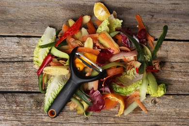 Photo of Peels of fresh vegetables and peeler on wooden table, top view