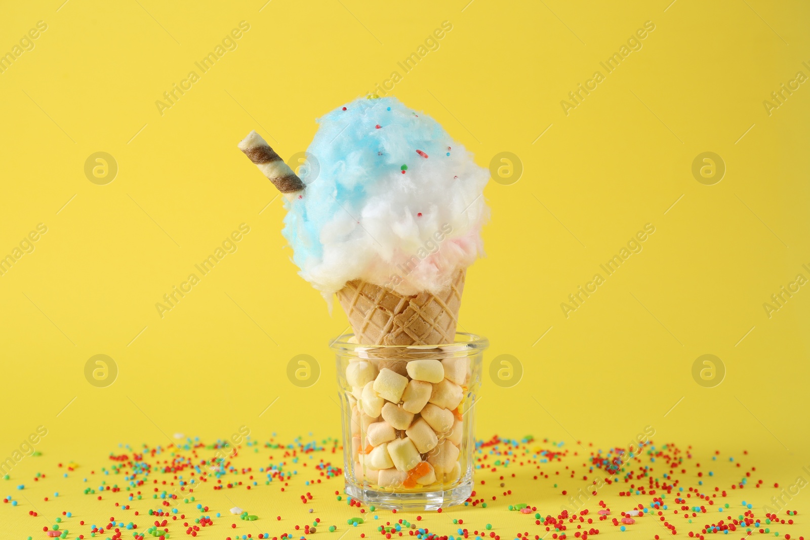 Photo of Sweet cotton candy in waffle cone on yellow background, closeup