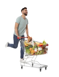 Photo of Happy man with shopping cart full of groceries on white background