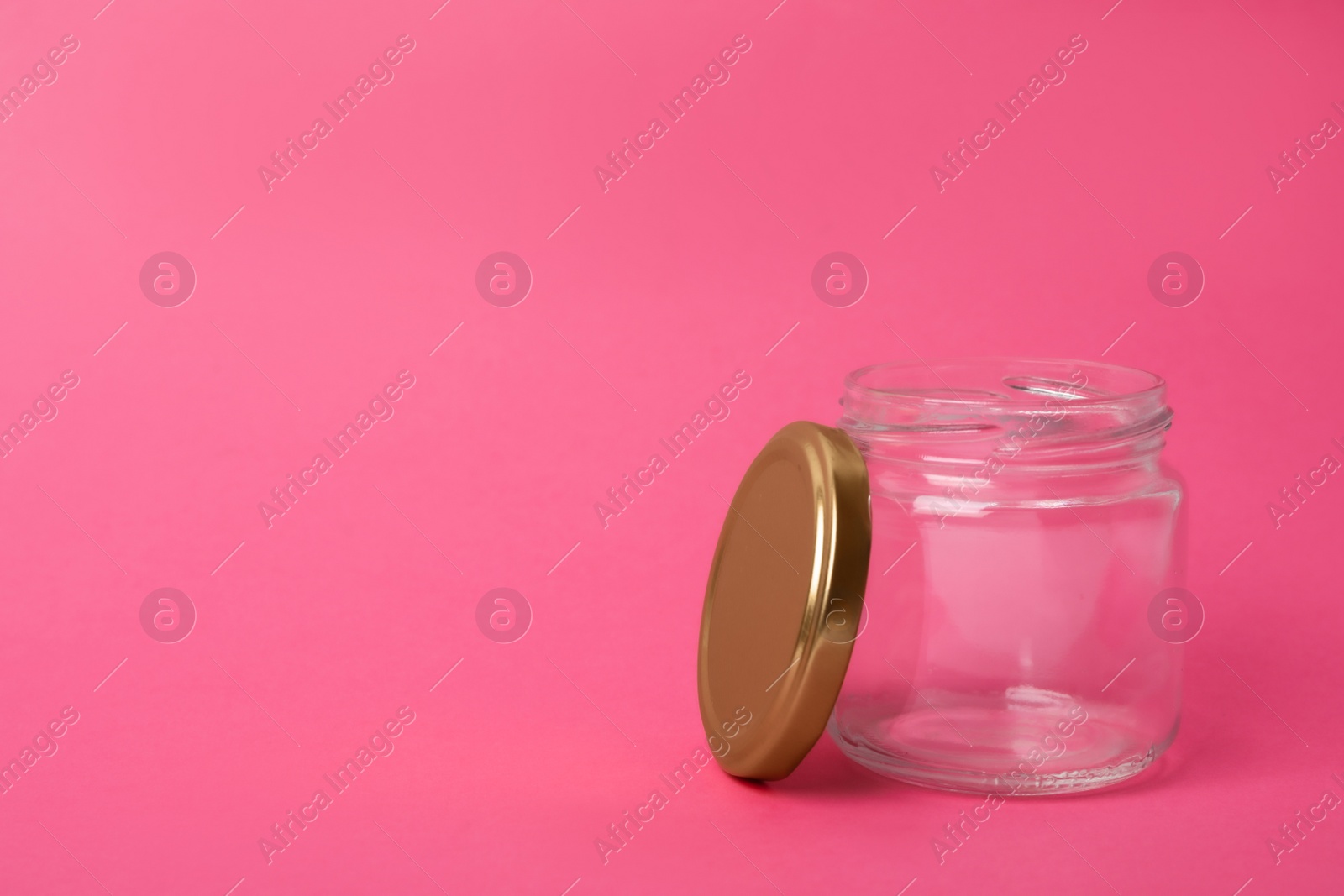 Photo of Open empty glass jar on pink background, space for text