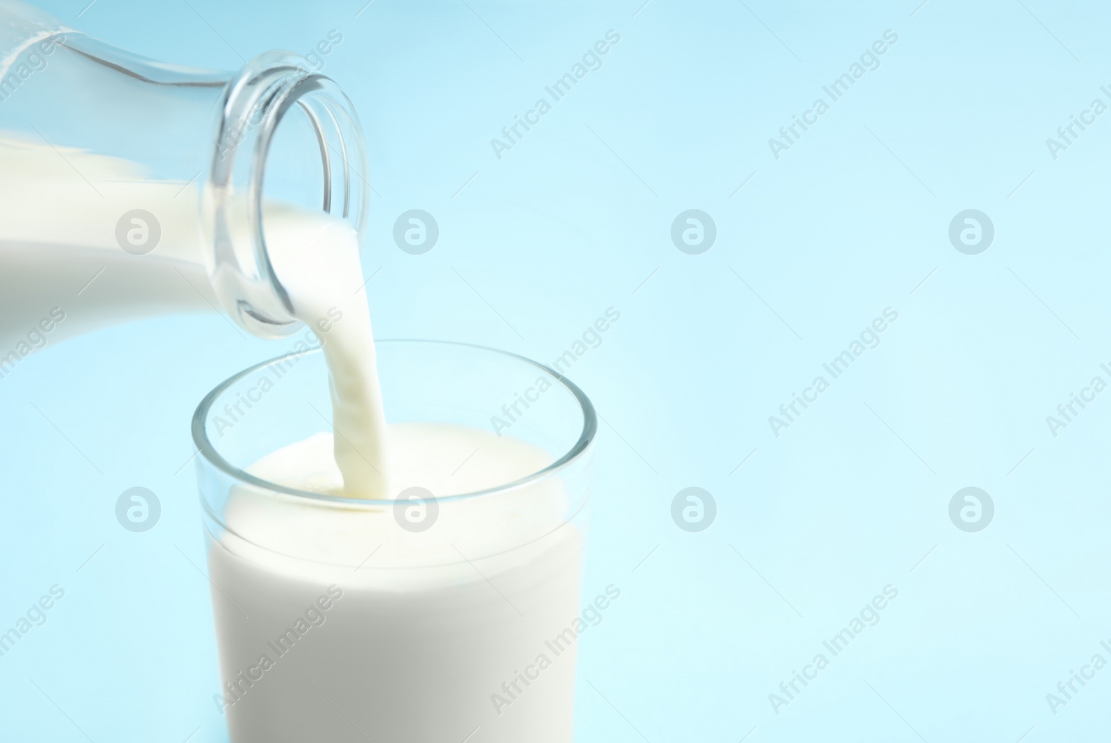 Photo of Pouring milk into glass on light blue background, closeup. Space for text