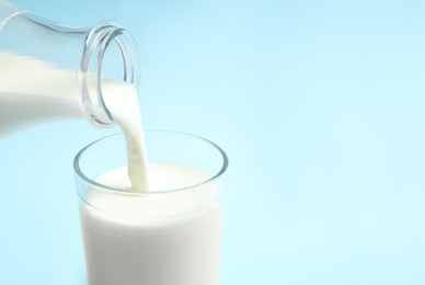 Photo of Pouring milk into glass on light blue background, closeup. Space for text