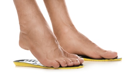 Man fitting orthopedic insoles on white background, closeup. Foot care