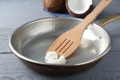 Frying pan with organic coconut cooking oil and spatula on grey wooden table, closeup