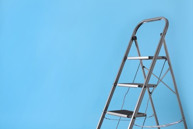 Photo of Metal stepladder on light blue background, space for text. Construction equipment