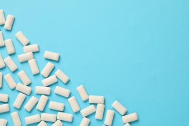 Photo of Many chewing gum pieces on light blue background, flat lay. Space for text