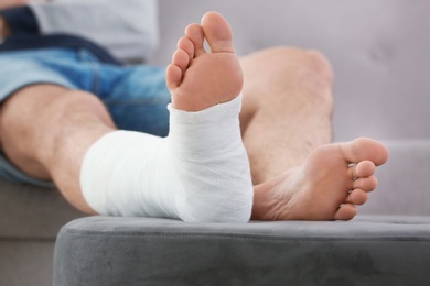 Photo of Young man with broken leg in cast sitting on sofa at home