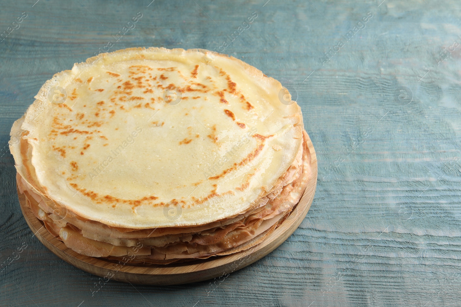 Photo of Stack of delicious crepes on blue wooden table. Space for text