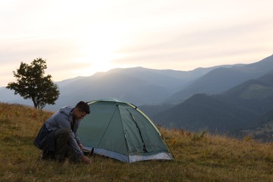 Photo of Man setting up camping tent in mountains at sunset