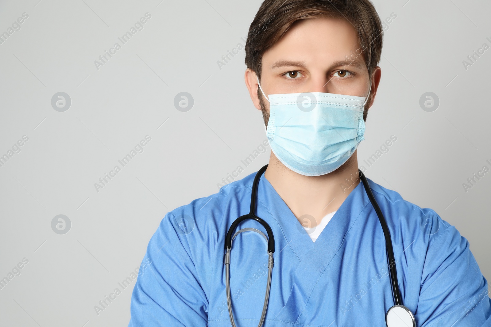 Photo of Doctor or medical assistant (male nurse) with protective mask and stethoscope on light grey background