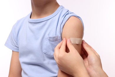 Woman sticking plaster on boy's arm after vaccination against white background, closeup